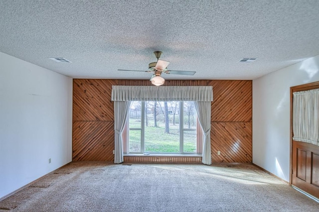 carpeted spare room featuring visible vents, a textured ceiling, and wood walls