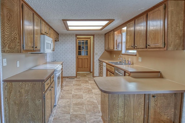 kitchen featuring wallpapered walls, a peninsula, white appliances, a textured ceiling, and a sink