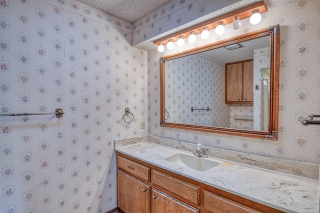 bathroom featuring wallpapered walls, vanity, and a textured ceiling