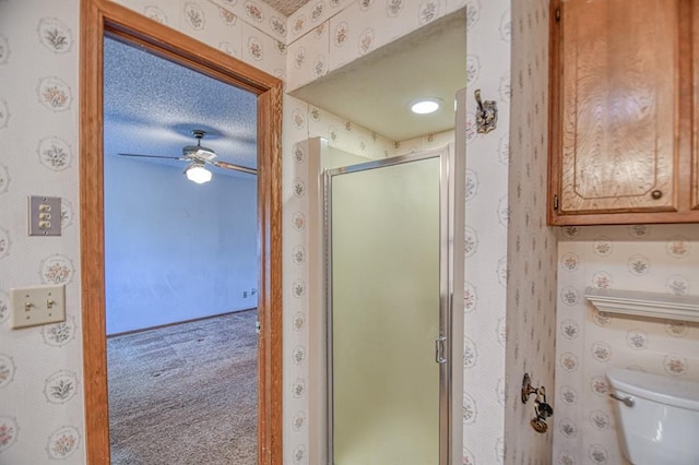 bathroom featuring ceiling fan, toilet, a stall shower, and wallpapered walls