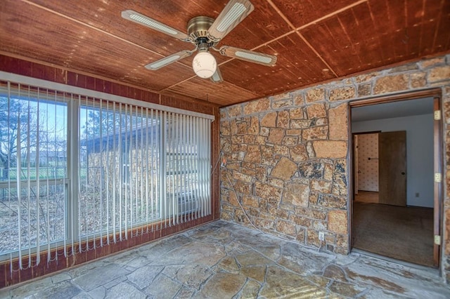 empty room featuring wooden ceiling, stone flooring, and a ceiling fan