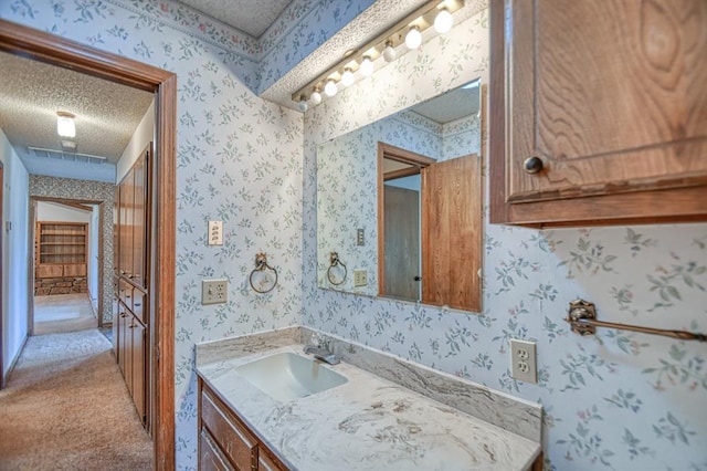 bathroom featuring visible vents, a textured ceiling, vanity, and wallpapered walls