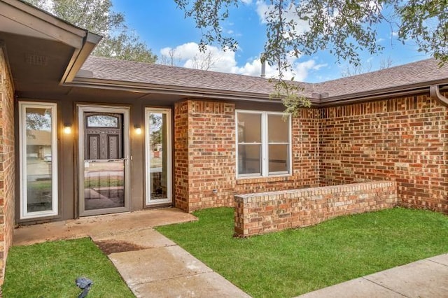 doorway to property featuring brick siding and a shingled roof