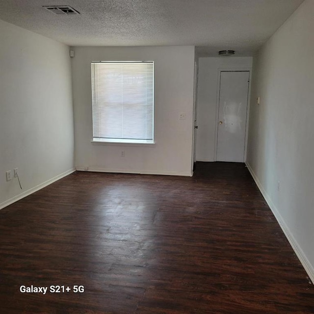 empty room with visible vents, a textured ceiling, baseboards, and wood finished floors