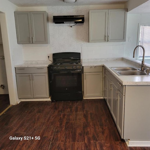 kitchen featuring light countertops, gray cabinetry, under cabinet range hood, a sink, and gas stove