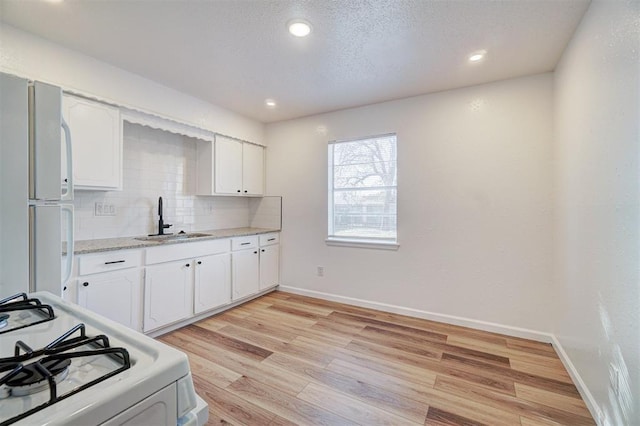 kitchen featuring white appliances, white cabinets, decorative backsplash, light wood-type flooring, and a sink