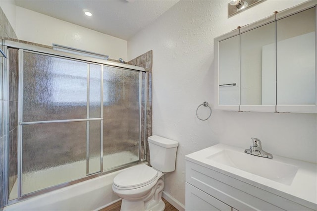 bathroom featuring toilet, a textured wall, enclosed tub / shower combo, and vanity