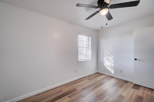 spare room featuring a textured ceiling, light wood finished floors, a ceiling fan, and baseboards