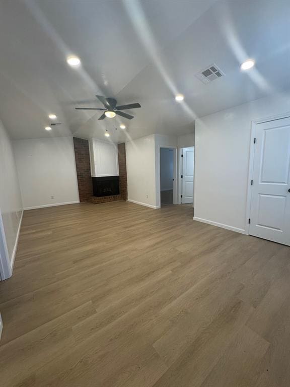 unfurnished living room with ceiling fan, wood finished floors, visible vents, baseboards, and a brick fireplace