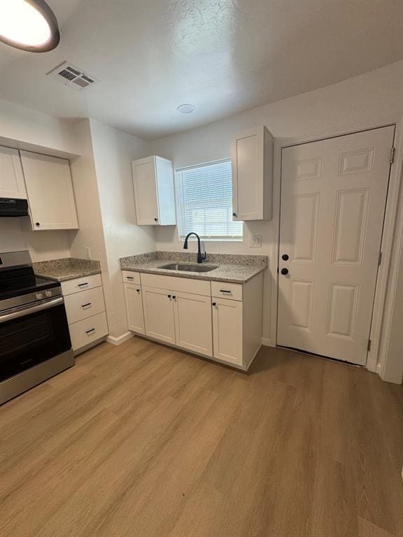 kitchen with visible vents, ventilation hood, stainless steel range with electric cooktop, light wood-style floors, and a sink