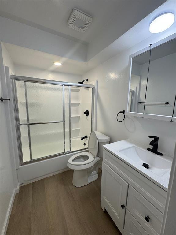 full bath featuring visible vents, toilet, shower / bath combination with glass door, wood finished floors, and vanity