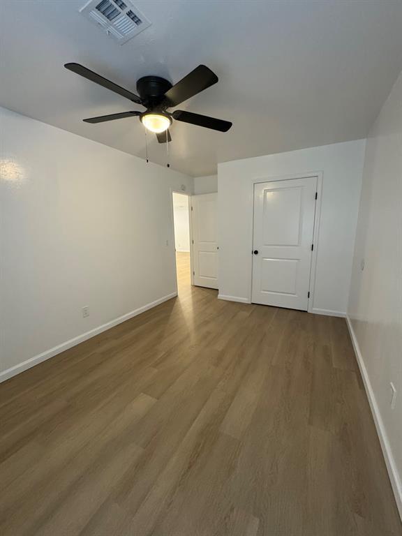 unfurnished room with a ceiling fan, visible vents, baseboards, and wood finished floors