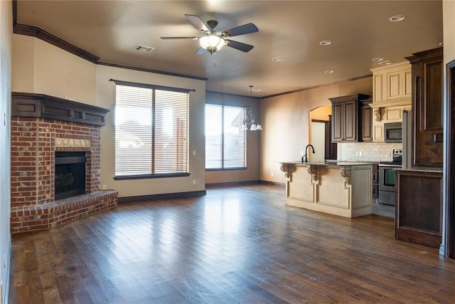 kitchen with a breakfast bar, crown molding, appliances with stainless steel finishes, a brick fireplace, and open floor plan