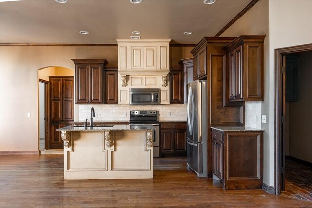 kitchen featuring arched walkways, decorative backsplash, light stone countertops, stainless steel appliances, and a sink