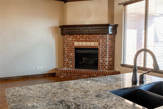 details featuring wood finished floors, a brick fireplace, a sink, and light stone countertops