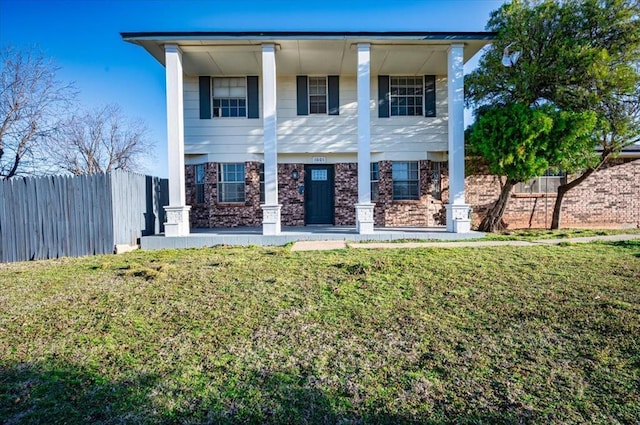 neoclassical home featuring stone siding, a front lawn, and fence