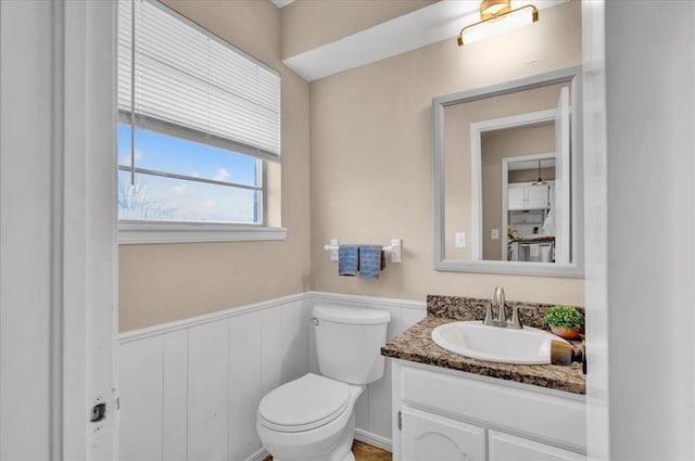 half bathroom featuring a wainscoted wall, toilet, and vanity