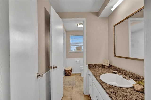 bathroom with tile patterned floors, wainscoting, toilet, and vanity