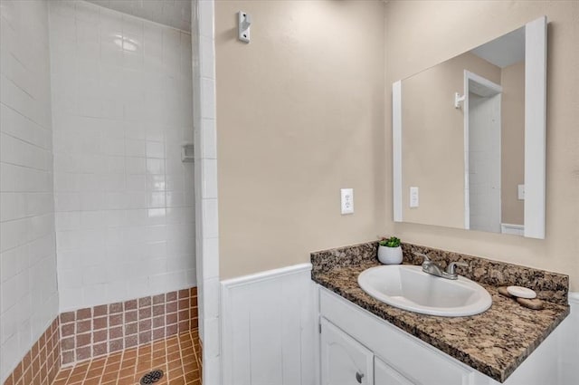 full bath with vanity, a wainscoted wall, and tiled shower