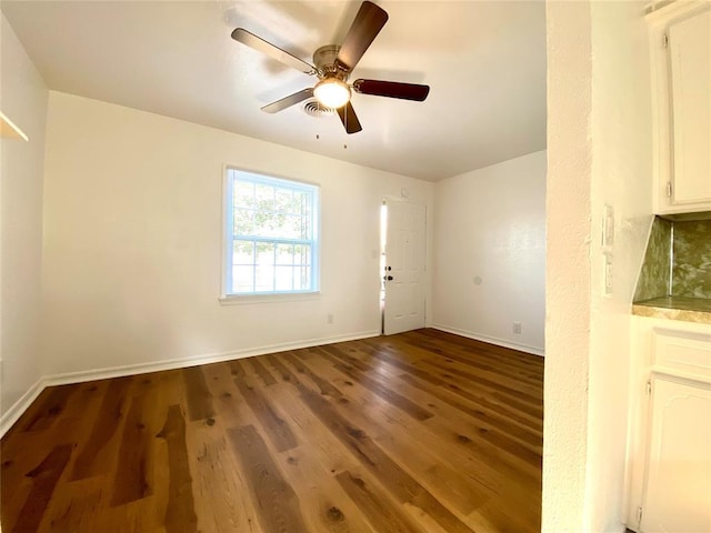 unfurnished room featuring a ceiling fan, visible vents, baseboards, and wood finished floors