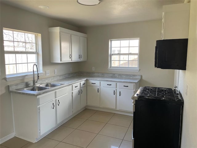 kitchen featuring gas range, light countertops, light tile patterned floors, white cabinets, and a sink