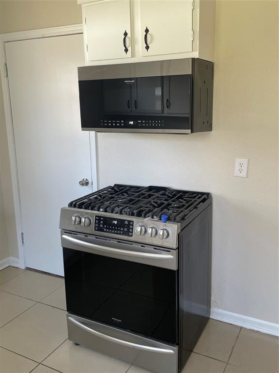 kitchen featuring light tile patterned floors, gas range, white cabinetry, and baseboards