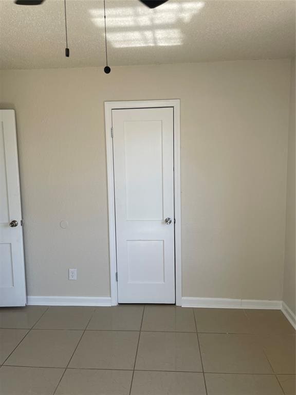 tiled empty room featuring baseboards and a textured ceiling