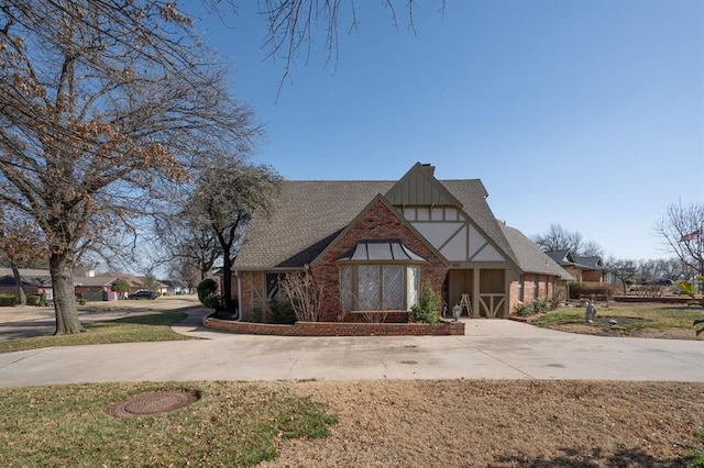 tudor home featuring brick siding, board and batten siding, a shingled roof, and a front yard