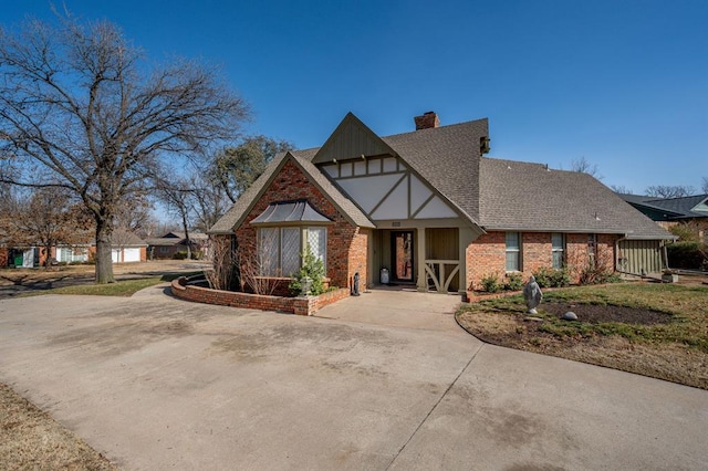 english style home featuring brick siding, concrete driveway, a chimney, and a shingled roof