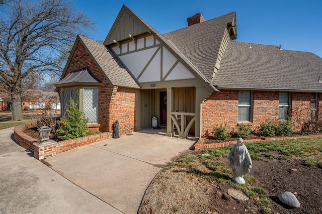 tudor house featuring brick siding, board and batten siding, a chimney, and a shingled roof