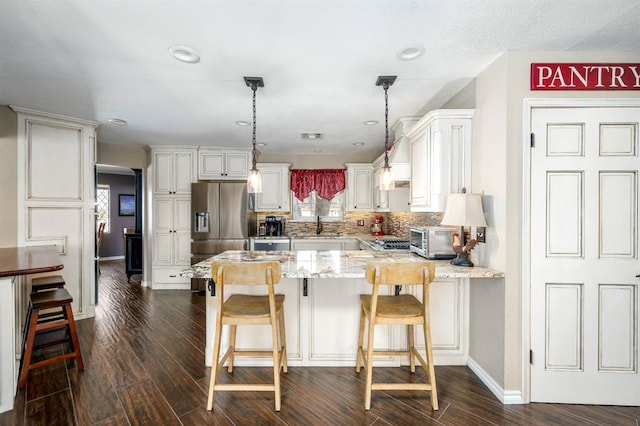 kitchen featuring a breakfast bar area, dark wood-style floors, a peninsula, stainless steel fridge, and backsplash