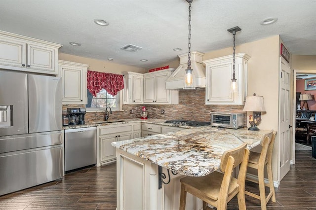 kitchen featuring visible vents, custom range hood, a peninsula, stainless steel appliances, and a sink