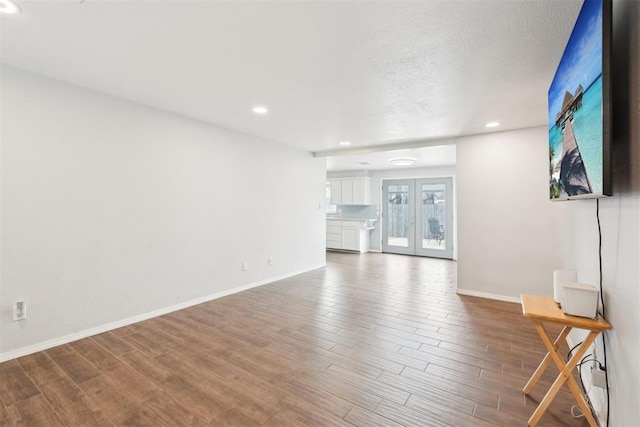 unfurnished living room featuring french doors, recessed lighting, a textured ceiling, wood finished floors, and baseboards