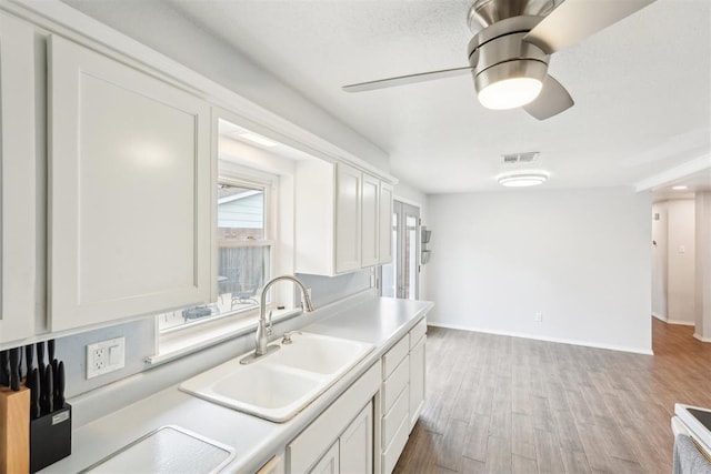 kitchen with light countertops, visible vents, white cabinets, a sink, and wood finished floors