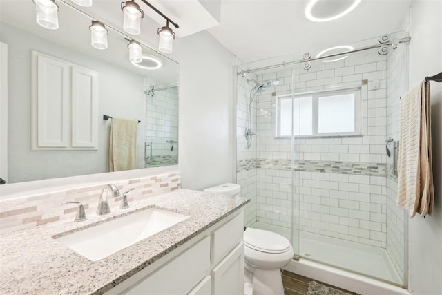 bathroom with toilet, a shower stall, decorative backsplash, and vanity