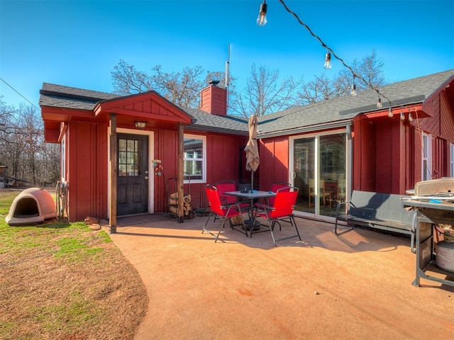 exterior space featuring outdoor dining area, a chimney, roof with shingles, board and batten siding, and a patio area