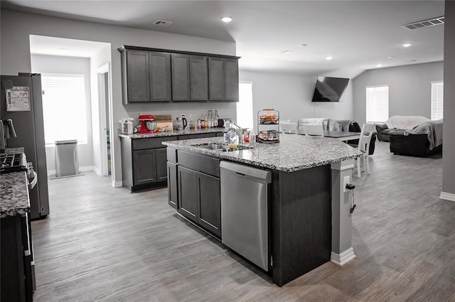 kitchen featuring light stone counters, stainless steel appliances, open floor plan, a sink, and light wood-type flooring