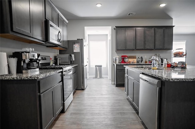 kitchen with stone countertops, a sink, visible vents, light wood-style floors, and appliances with stainless steel finishes