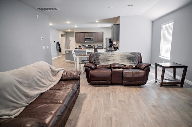 living room with lofted ceiling, light wood-style flooring, visible vents, and baseboards