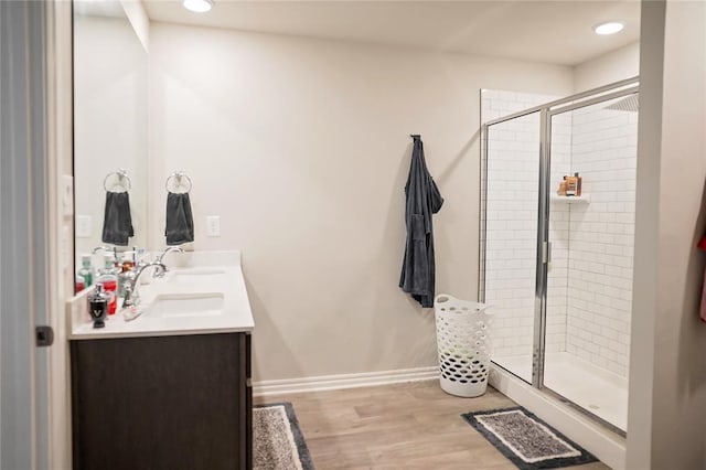 bathroom featuring double vanity, baseboards, wood finished floors, a shower stall, and a sink