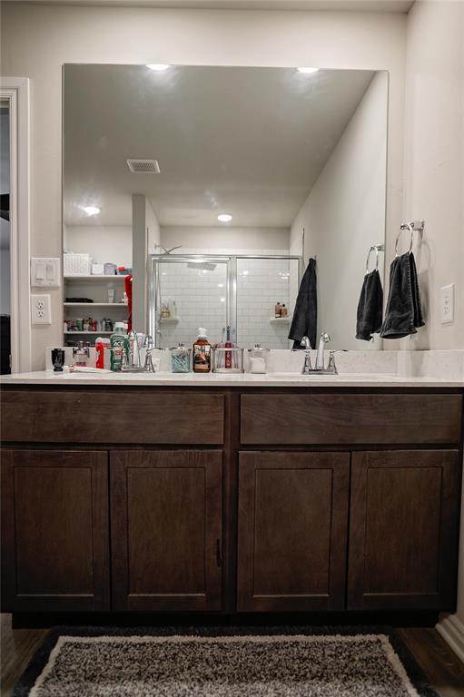 full bath featuring a sink, wood finished floors, visible vents, double vanity, and a stall shower