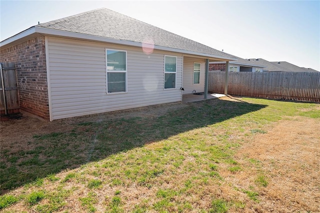 rear view of property with brick siding, a shingled roof, fence, a lawn, and a patio area