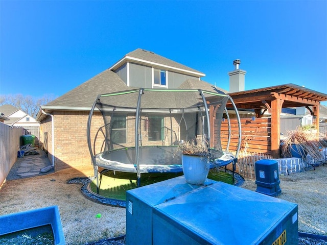 exterior space with brick siding, a trampoline, roof with shingles, a chimney, and a fenced backyard