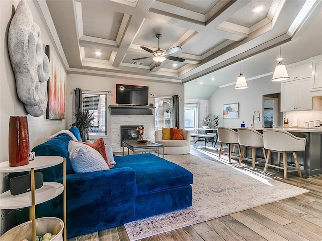 living room featuring ornamental molding, beam ceiling, a fireplace, wood finished floors, and coffered ceiling