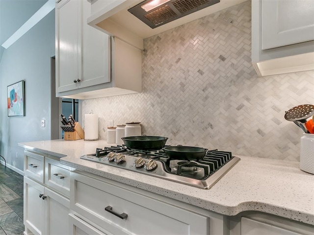 kitchen with light stone counters, white cabinetry, exhaust hood, decorative backsplash, and stainless steel gas cooktop