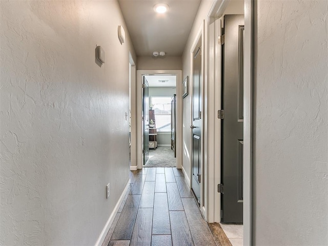 corridor featuring baseboards and a textured wall