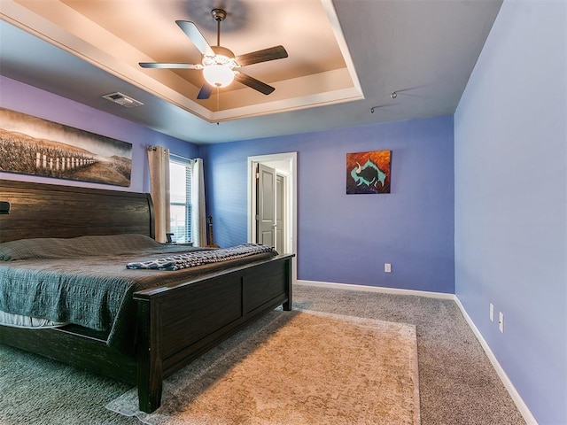 carpeted bedroom featuring visible vents, baseboards, a tray ceiling, and a ceiling fan