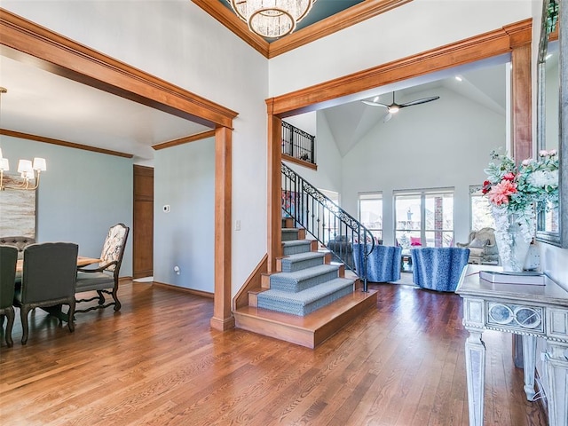 interior space with baseboards, wood finished floors, crown molding, high vaulted ceiling, and ceiling fan with notable chandelier