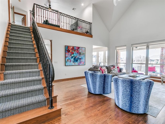 living room featuring visible vents, baseboards, wood finished floors, stairs, and high vaulted ceiling