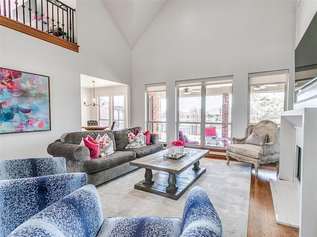 living room featuring a chandelier, high vaulted ceiling, a fireplace with raised hearth, and wood finished floors